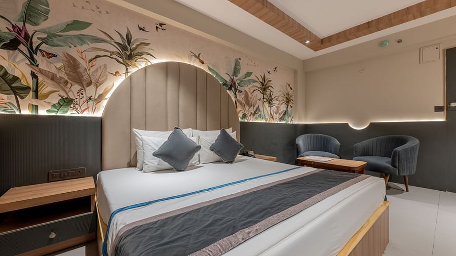 A room with king size bed, ceiling fan, floral mural wall, and grey chairs at Hotel Highway King, Jaipur.