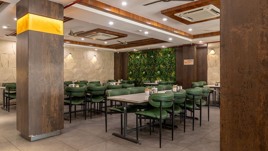 Indoor dining section with polished flooring, ceiling lighting, and seating arrangement with green chairs at Hotel Highway King, Jaipur.