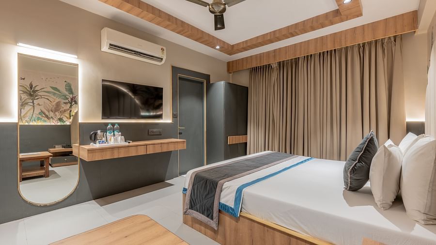 A spacious room with a king size bed, TV, mirror, desk, and the curtain spread across the window at Hotel Highway King, Jaipur.