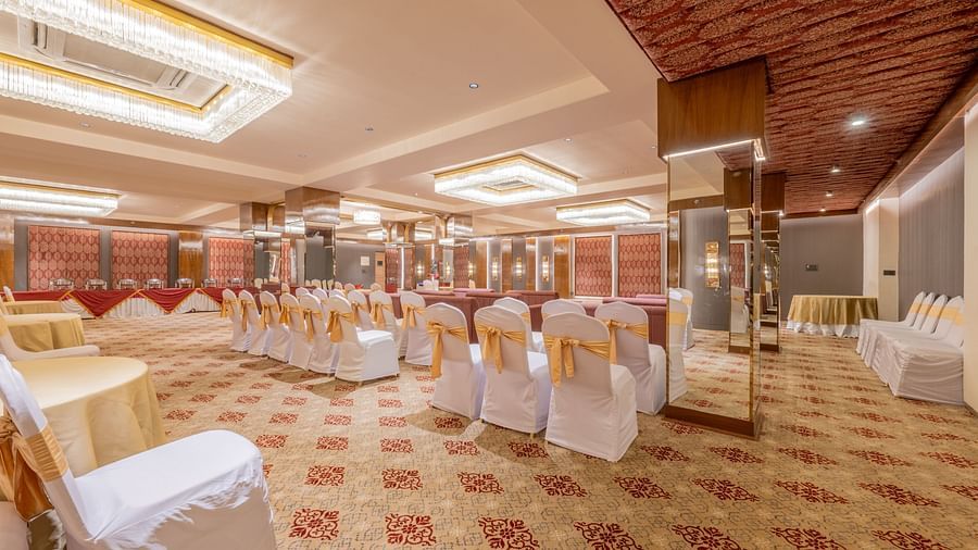 Rows of white-covered banquet chairs with gold ribbons facing a decorated stage area inside a well-lit hall at Hotel Highway King, Jaipur.