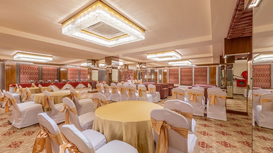 Round tables with yellow tablecloths and white chairs arranged under a decorative ceiling light at Hotel Highway King, Jaipur.