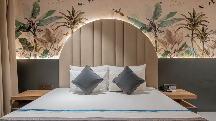 A front-facing view of bed with arched padded headboard and tropical-themed wall mural at Hotel Highway King, Jaipur.