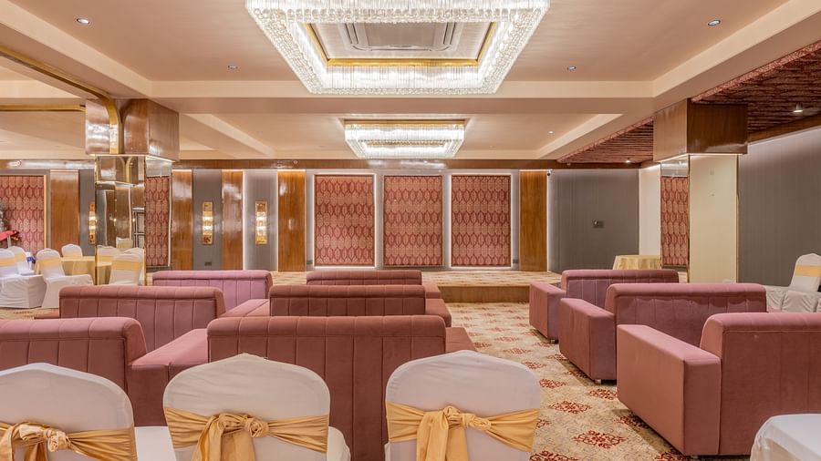 A view of the banquet area with maroon sofas and chairs neatly arranged under elegant ceiling lights at Hotel Highway King, Jaipur.