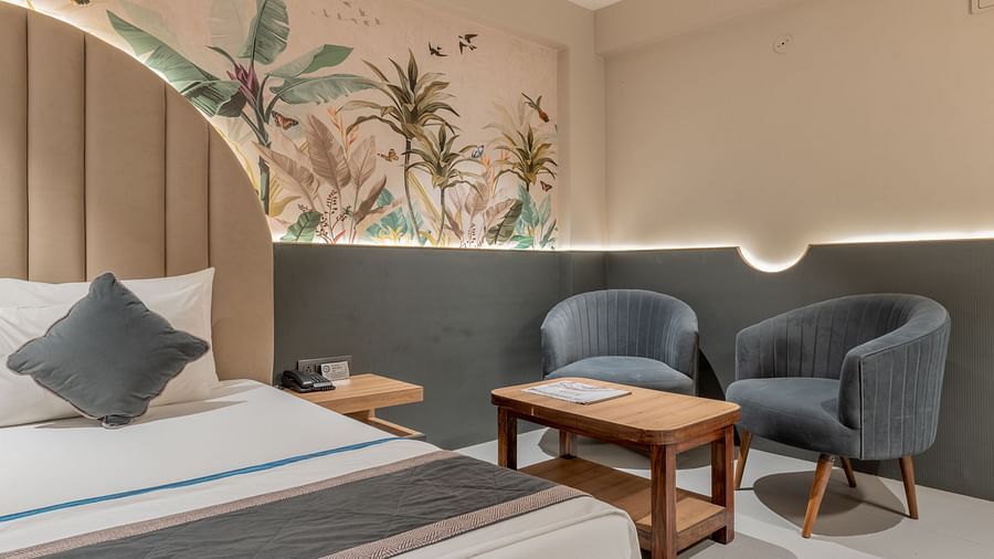 A seating area with grey chairs and wooden table beside bed and floral wall design at Hotel Highway King, Jaipur.