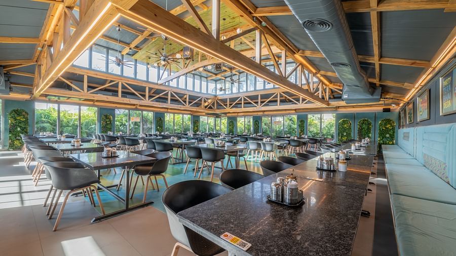 Restaurant seating area with black tables and chairs, wooden beams, and large windows at Hotel Highway King, Jaipur.