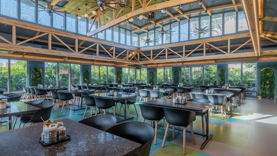 Spacious dining hall with black tables, wooden rafters, and full-length windows at Hotel Highway King, Jaipur.