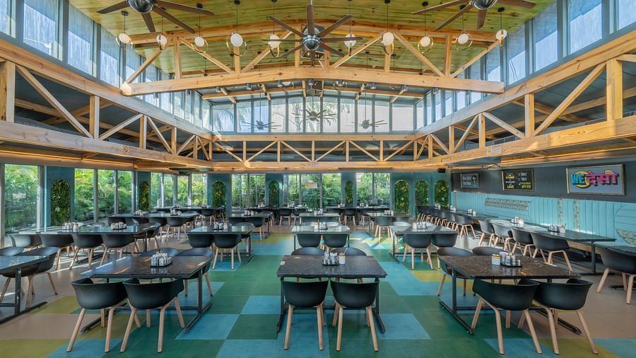 Bright dining area with black chairs, yellow ceiling beams, and large windows at Hotel Highway King, Jaipur.