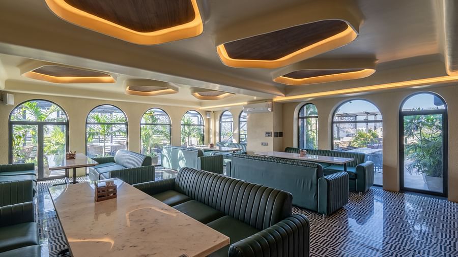 Lounge dining space with marble tables, green seating, and arched glass windows at Hotel Highway King, Jaipur.