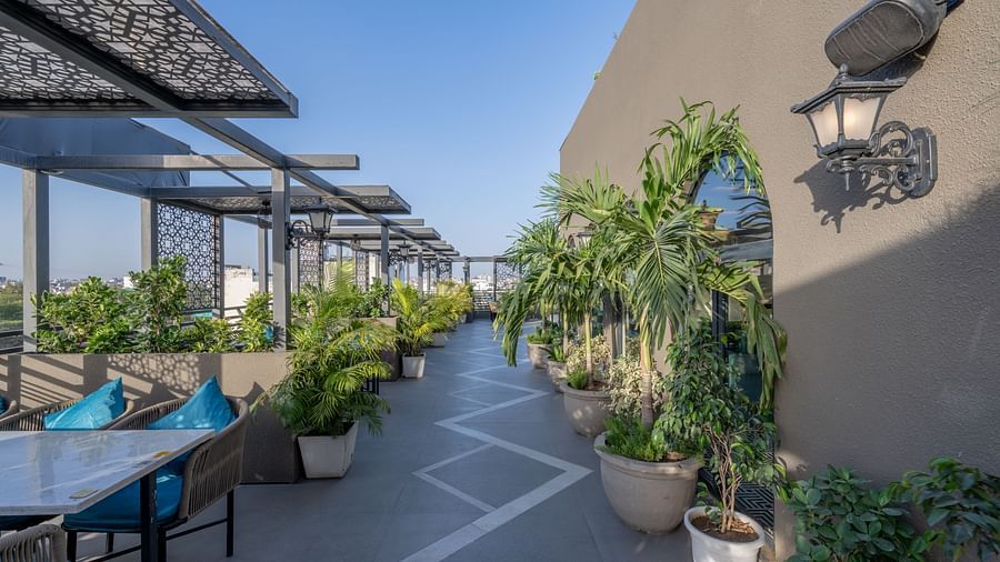Outdoor terrace dining space with blue table setups, potted plants, and wall lanterns at Hotel Highway King, Jaipur.