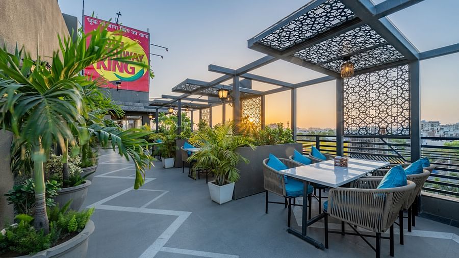 Rooftop dining area with King’s signage, lattice screens, and potted plants and trees at Hotel Highway King, Jaipur.
