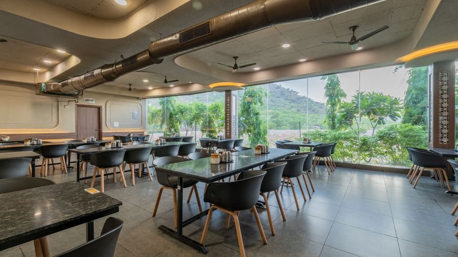 Restaurant interior showing a dining space and panoramic window view of the surrounding hills at Hotel Highway King, Neelka.