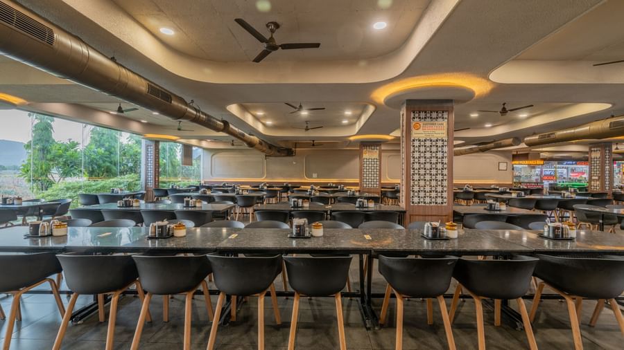 Chairs neatly arranged around a table with a glass panel to the side, offering a view of the lawn at Hotel Highway King, Neelka.