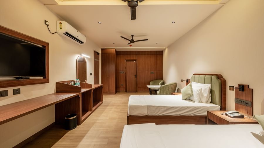 Spacious room with twin beds, wooden furnishings, wall-mounted TV, dressing mirrors, two ceiling fans, and air conditioning at Hotel Highway King, Neemrana.