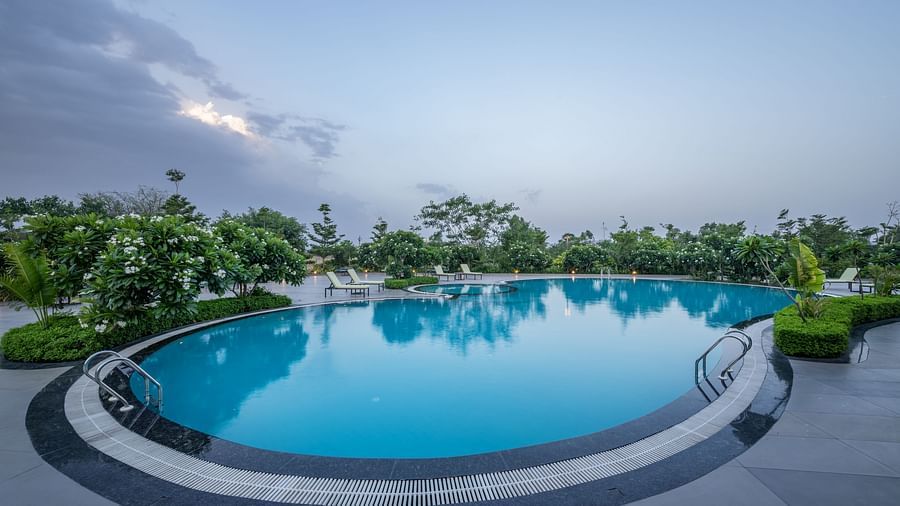 The inviting swimming pool surrounded by pathways and greenery at Hotel Highway King Shahpura under a cloudy sky.