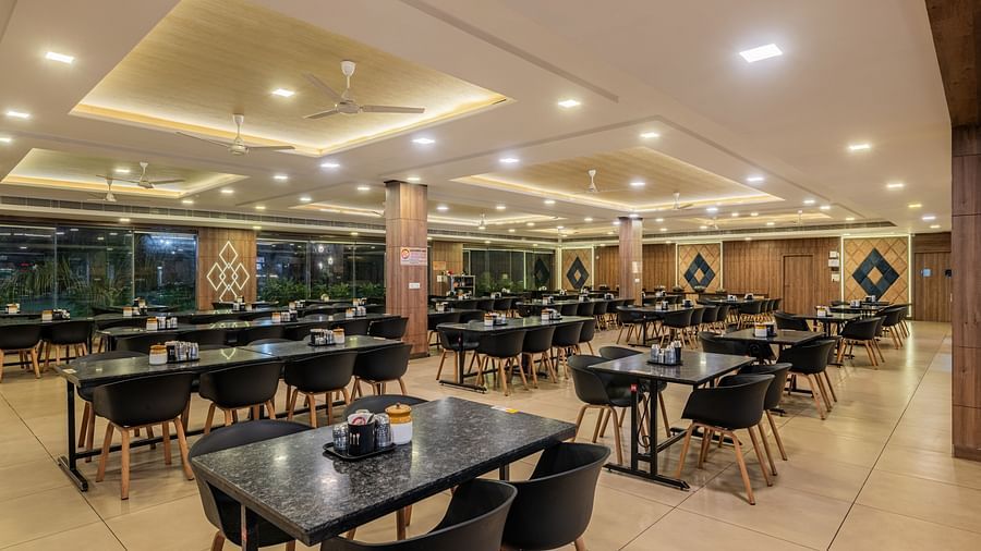 An empty, well-lit dining area inside the Hotel Highway King Shahpura, set with numerous tables and chairs.