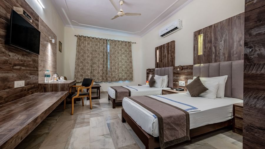 A spacious guest room with multiple beds and a TV at Hotel Highway King Shahpura.