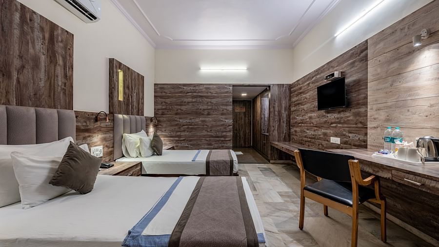 A long view of a guest room at Hotel Highway King Shahpura with multiple beds and a desk area.