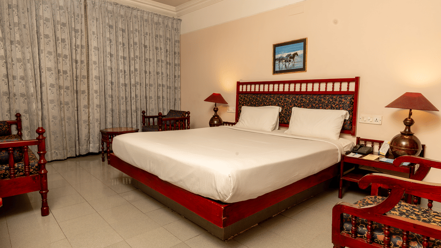 A bedroom with a queen size bed, red wooden headboard, and matching bedside furniture at Hotel Horizon, Trivandrum.