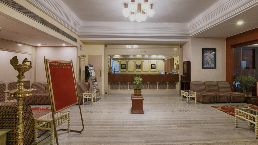 A spacious lobby with marble floors, a reception desk in the background, and a traditional brass floor lamp in the foreground at Hotel Horizon, Trivandrum.