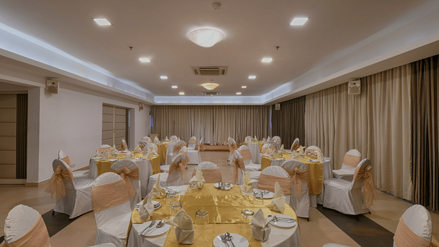 A large, formal banquet hall set with round tables, white chairs with gold bows, and soft overhead lighting at Hotel Horizon, Trivandrum.