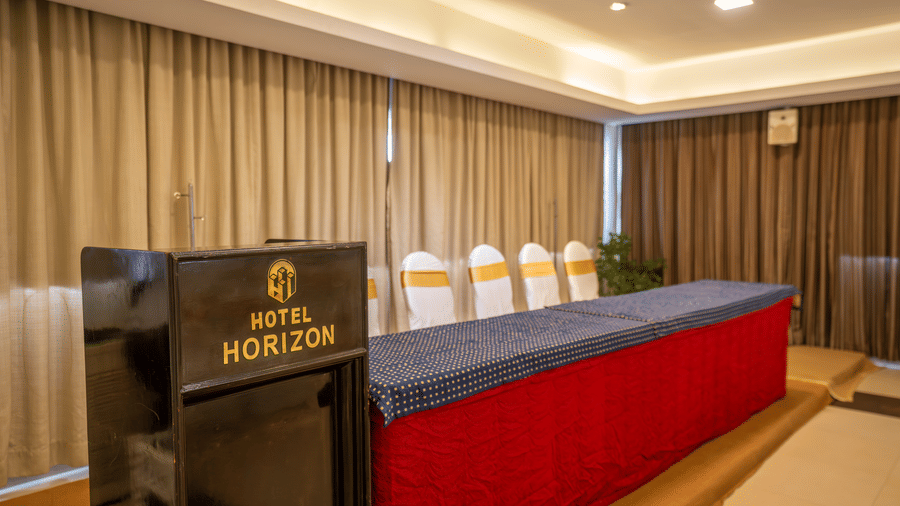 A podium labelled 'Hotel Horizon' sits in front of a blue and red draped table in a conference room with beige curtains at Hotel Horizon, Trivandrum.