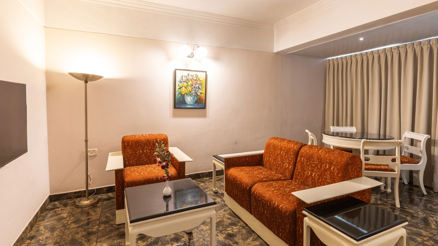 A suite featuring a living area with red sofa and armchair with a dining table in the background at Hotel Horizon, Trivandrum.