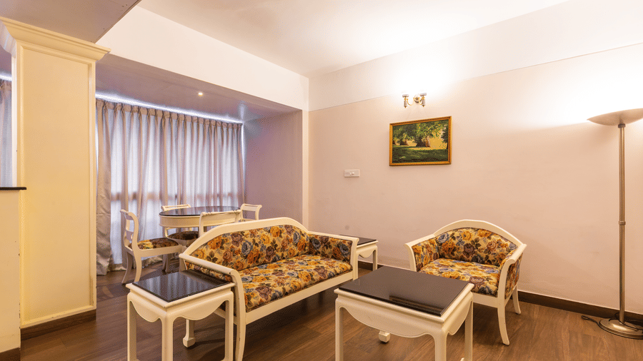 A living room with floral-patterned armchairs, black tables, a wall art, and chairs arranged around white coffee tables at Hotel Horizon, Trivandrum.