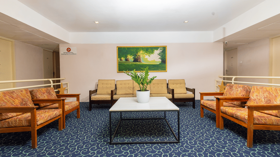 A lobby area featuring orange patterned armchairs and a white coffee table on a blue patterned carpet at Hotel Horizon, Trivandrum.