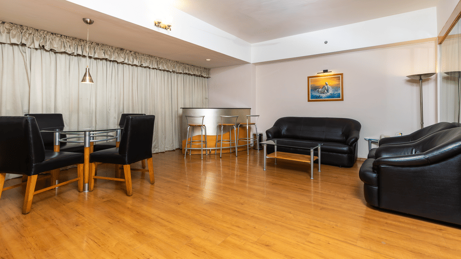 A minimalist lounge with polished wood floors, black leather sofas, a glass coffee table, and beige curtains at Hotel Horizon, Trivandrum.