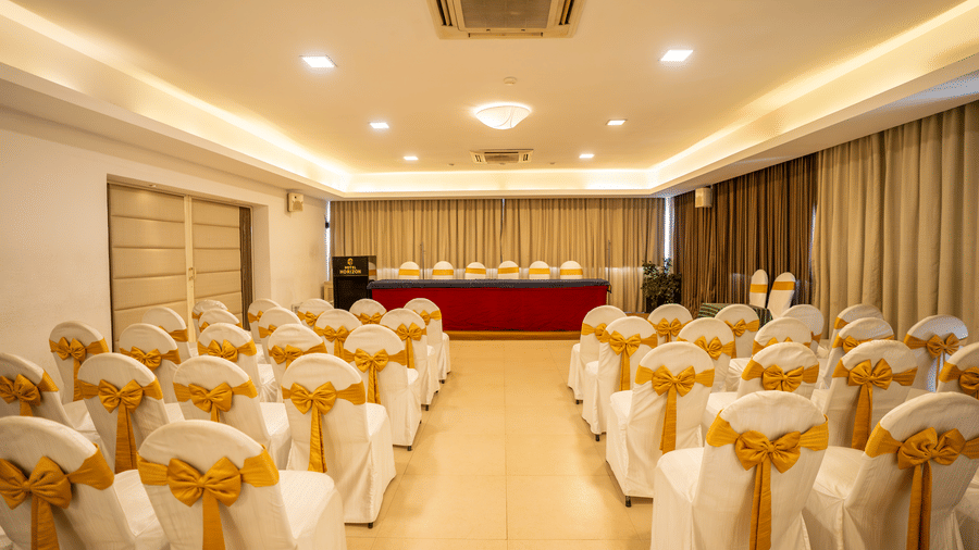 An indoor banquet hall arranged with rows of white chairs with gold ribbons facing a stage at Hotel Horizon, Trivandrum.