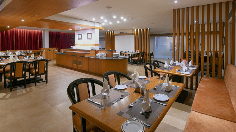 A restauratn featuring wooden tables and chairs, a buffet counter in the background, and wooden slat room dividers at Hotel Horizon, Trivandrum.