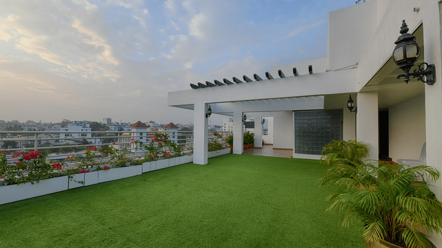 An outdoor rooftop area featuring artificial green garden, white walls, and a view of a city at Hotel Horizon, Trivandrum.