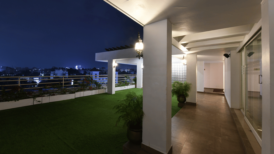 A rooftop terrace at night with green turf, white pillars, and a lit walkway overlooking city lights at Hotel Horizon, Trivandrum.