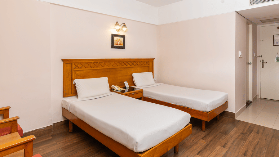 A room with 2 single beds, light wood headboards, a wall art, and a view of the entry door at Hotel Horizon, Trivandrum.