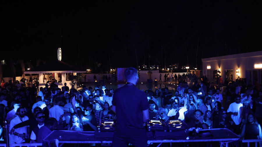 Crowded night-time event with people dancing, focused on a DJ console under bright blue stage lighting at Hotel Hukam's Lalit Mahal.