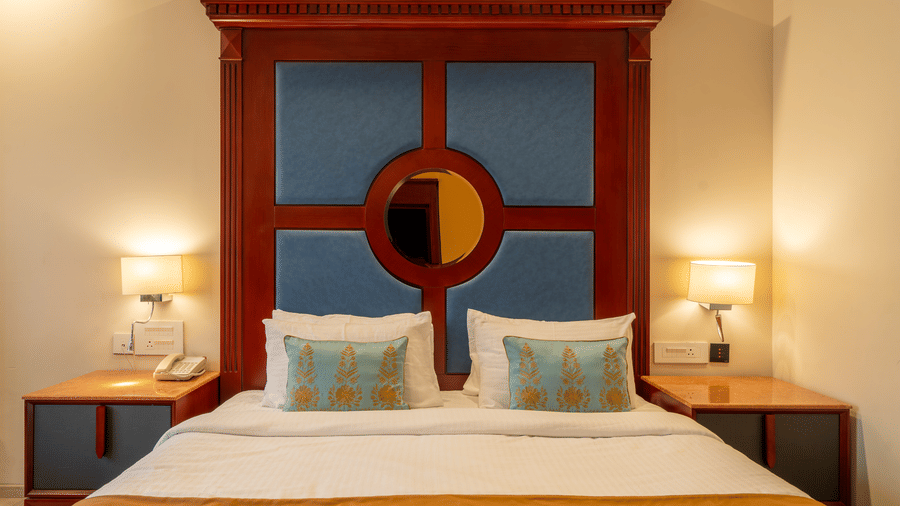 Close-up of a double bed with pillows, flanked by lamps and a striking blue and mahogany headboard design at Hotel Hukam's Lalit Mahal.