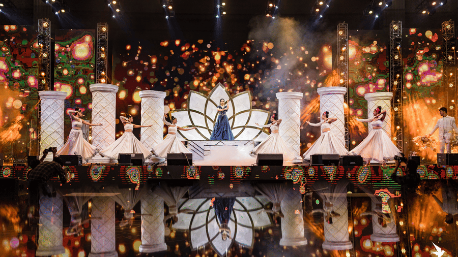 A dark stage background with glowing, ornate decor elements and intense warm stage lighting and sparkling effects at Hotel Hukam's Lalit Mahal.