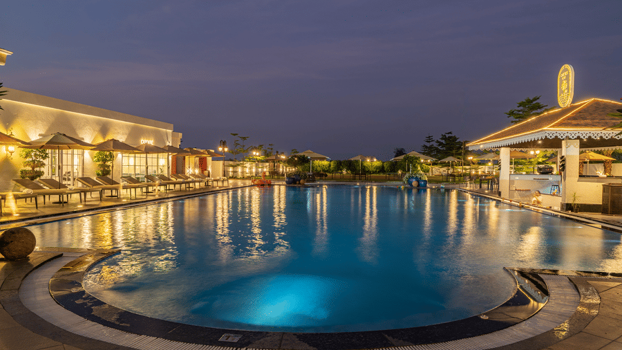 Outdoor swimming pool and surrounding buildings lit gently at dusk or early night, reflecting the sky and lights at Hotel Hukam's Lalit Mahal