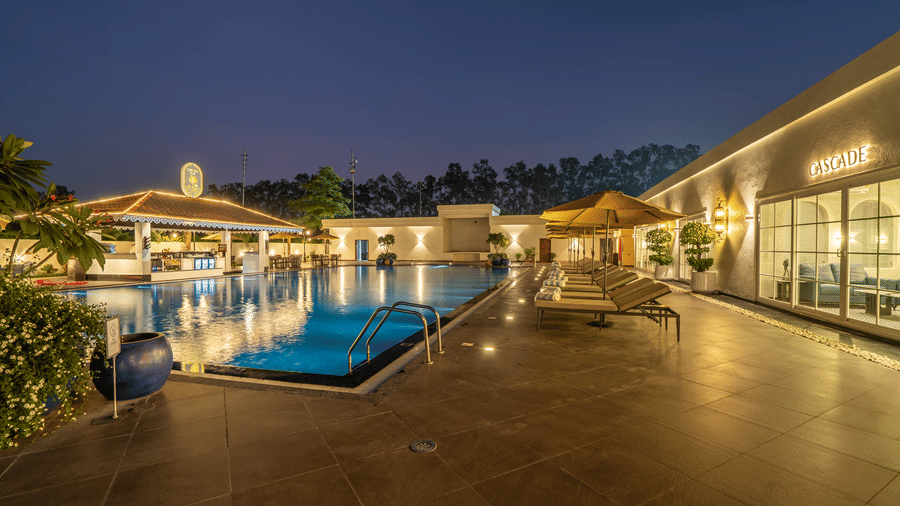 Outdoor pool area at night with blue water and ambient warm lighting illuminating the surrounding deck and buildings at Hotel Hukam's Lalit Mahal.