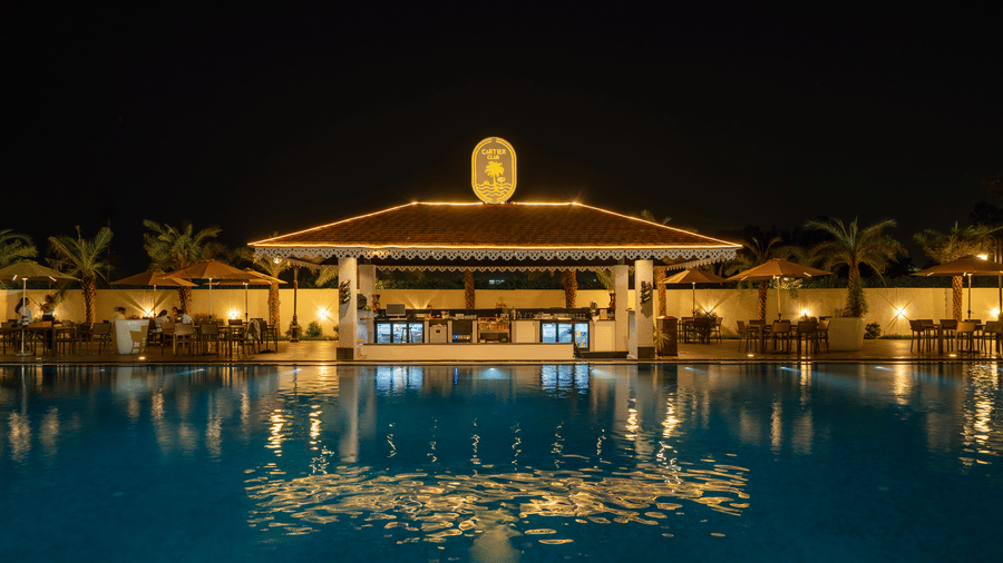 Poolside bar pavilion with its reflection visible in the calm, dark water of the swimming pool at night at Hotel Hukam's Lalit Mahal.