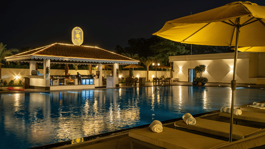 Evening view of the swim-up bar area next to the pool, featuring seating and ambient lighting under an umbrella at Hotel Hukam's Lalit Mahal.
