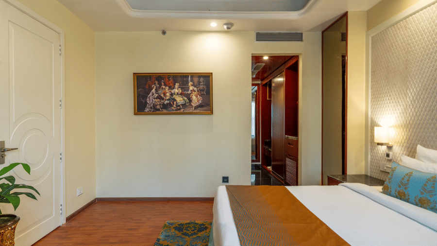 Spacious hotel room with a large bed, picture frames on the wall, and detailed white wall panelling at Hotel Hukam's Lalit Mahal.