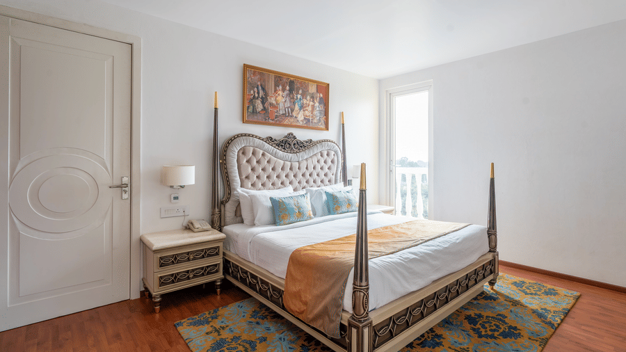 Elegant bed with a tufted headboard, ornate wooden frame, and a colourful painting above the bed at Hotel Hukam's Lalit Mahal.