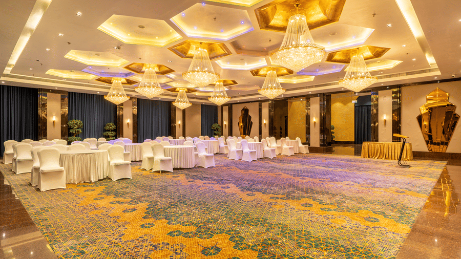 Wide view of a long banquet table covered in white cloth, set up under ornate gold and white hexagonal chandeliers at Hotel Hukam's Lalit Mahal.