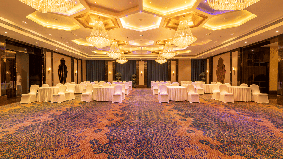 Grand banquet hall with a patterned carpet, dark walls, and stunning hexagonal crystal chandeliers on the ceiling at Hotel Hukam's Lalit Mahal.