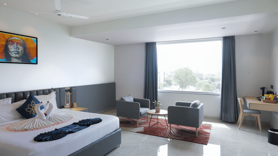 A hotel room at Hotel Kyzen HiTech City featuring a king bed with white bedding grey headboard large windows with grey curtains a work desk and a Buddha artwork on the wall.