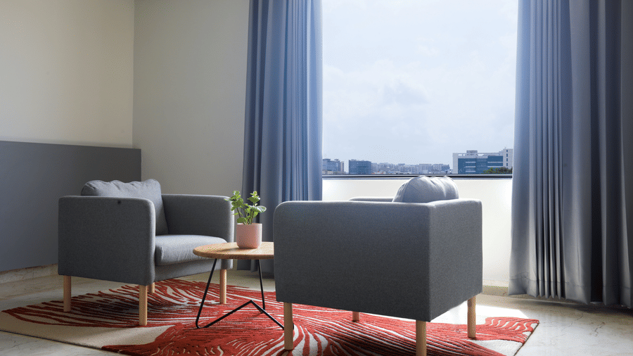 Comfortable grey sofa chairs with blue curtains and plant in Deluxe Room at Hotel Kyzen HiTech City – Your Zenly Stay.