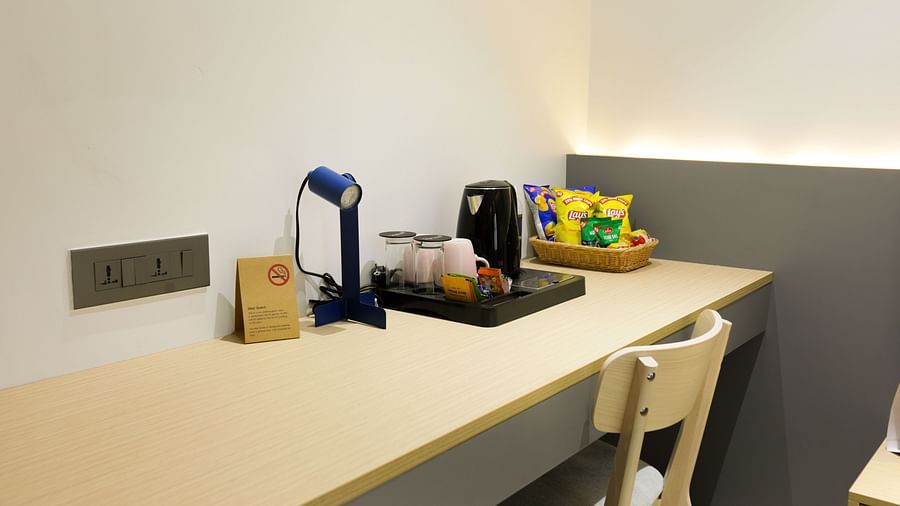Long study desk with kettle, cups, and welcome kit against a white wall at Hotel Kyzen HiTech City – Your Zenly Stay.