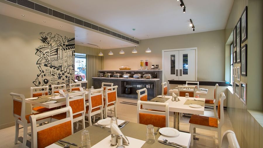 A modern and well-lit buffet restaurant interior with white chairs and orange cushions - Hotel Langford Keys by TGI, Shanti Nagar