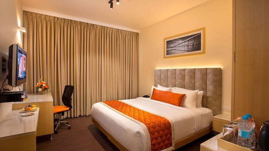A cosy hotel room with a plush bed adorned with an orange bed runner, a work desk and a wall-mounted TV - Hotel Langford Keys by TGI, Shanti Nagar